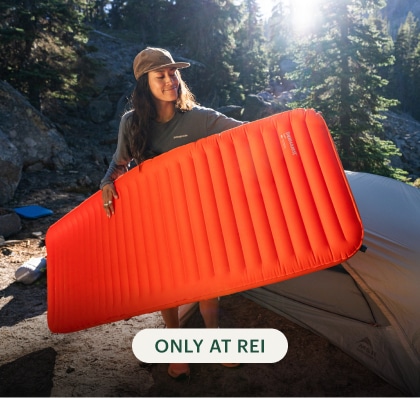 A person smiling carries a Therm-a-Rest sleeping pad.