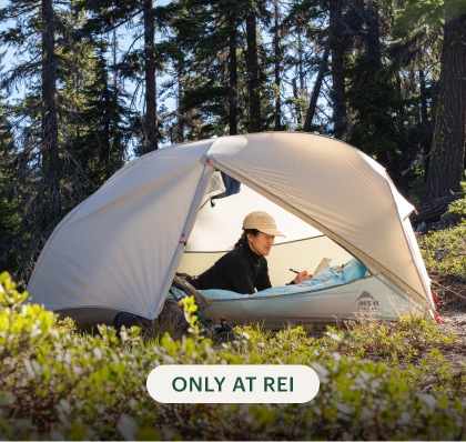 A camper journals in their M S R tent set up in a meadow.