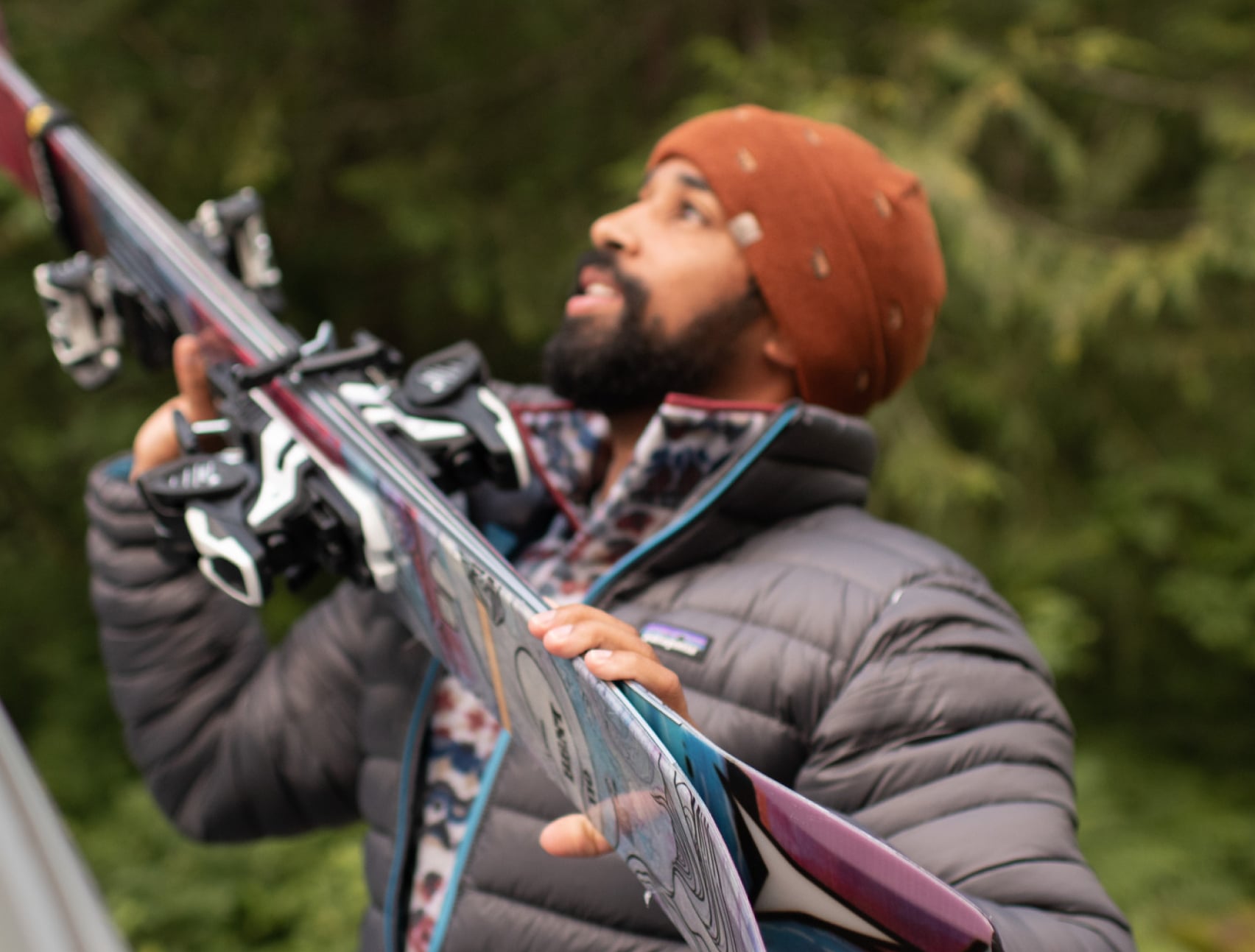 A person wearing a comfy puffy jacket while lifting skis onto a car rack.