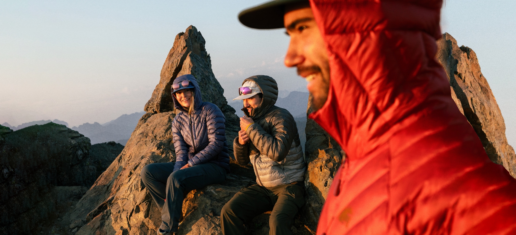 Three hikers in R E I Co-op brand gear take a break on a summit trail.