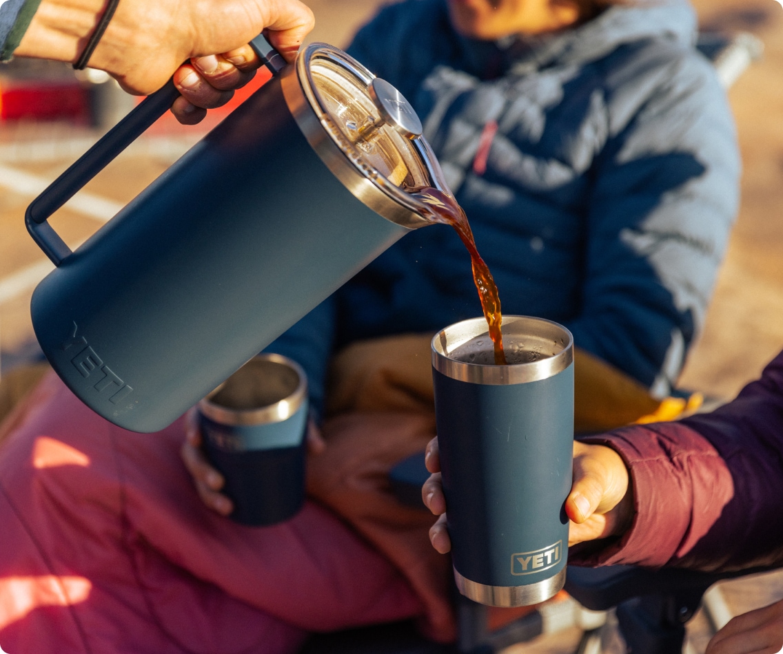 A camper pours coffee from a YETI French press into a YETI tumbler.