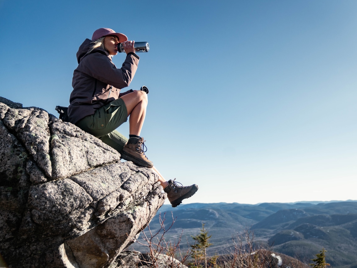 A hiker takes a break on a rock while drinking from a YETI water bottle.