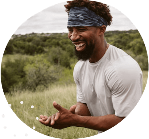 A smiling portrait of a black man clapping in a meadow.