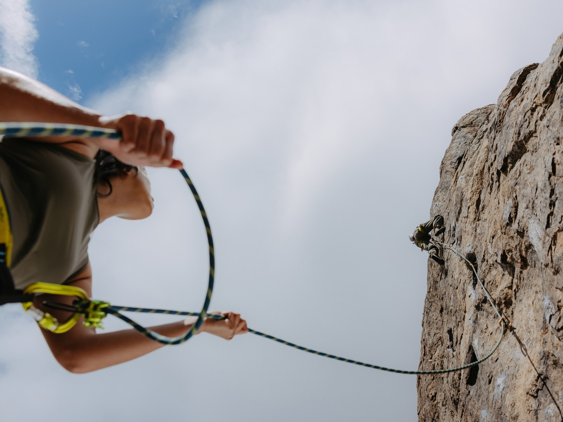 A person belays a climber on a rock face.