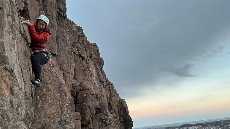 A person rock climbs with an overcast sky