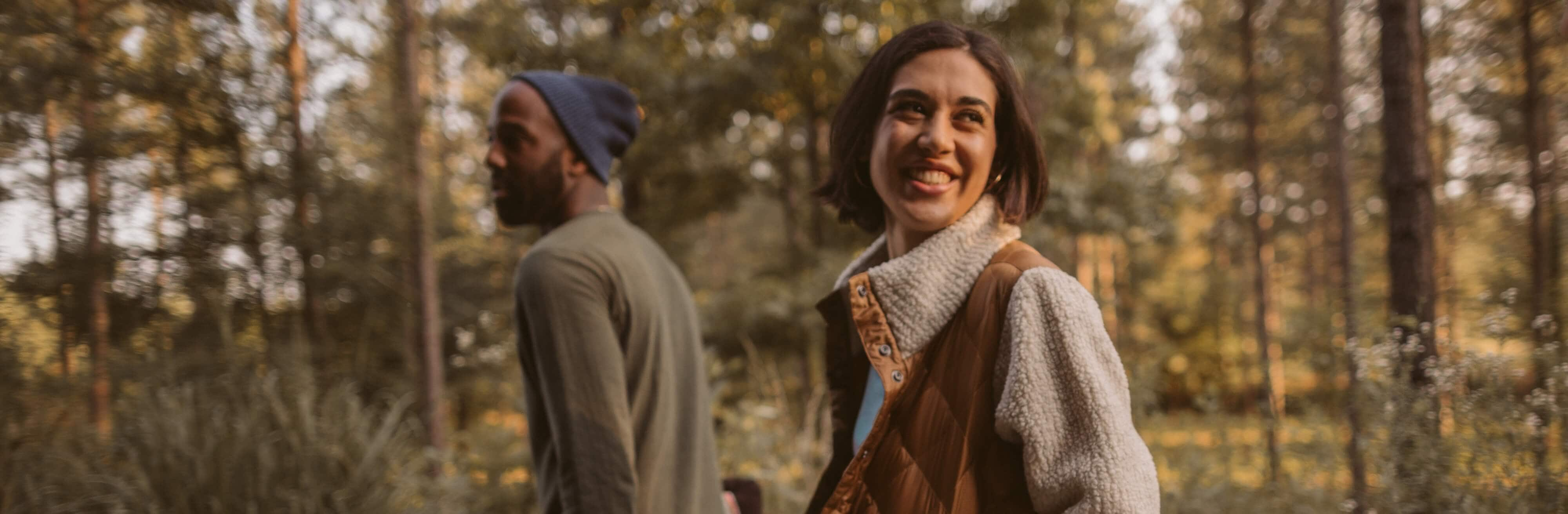 Two people walk through the woods in the waning golden sunlight of a fall evening.