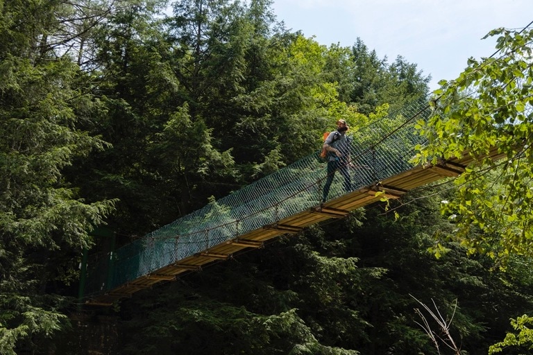 A hiker crosses a wooded trail along a bridge