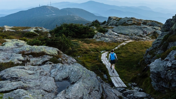 A hiker walks on a boardwalk trail through rocky outcroppings