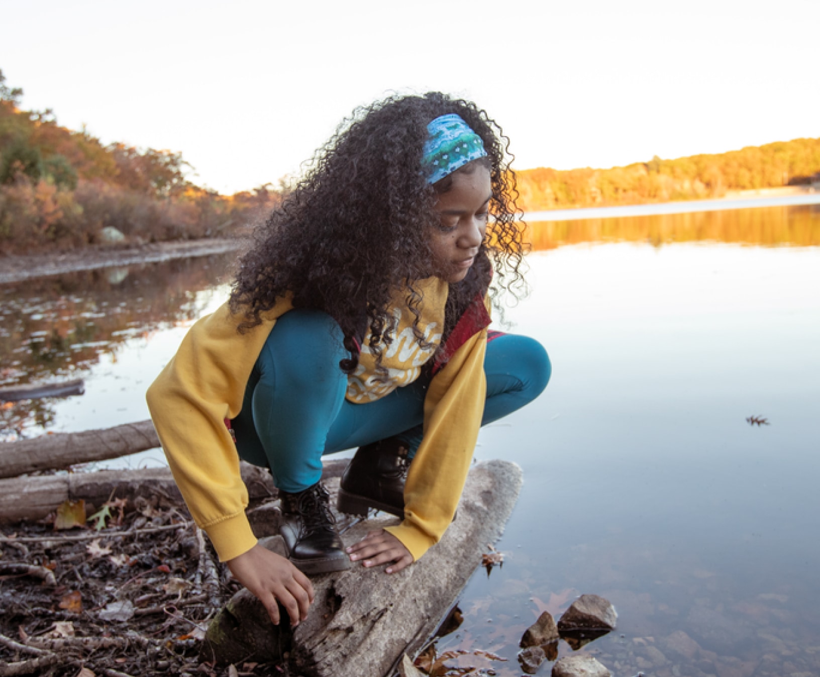 A child crouching on a log by a tranquil lake.