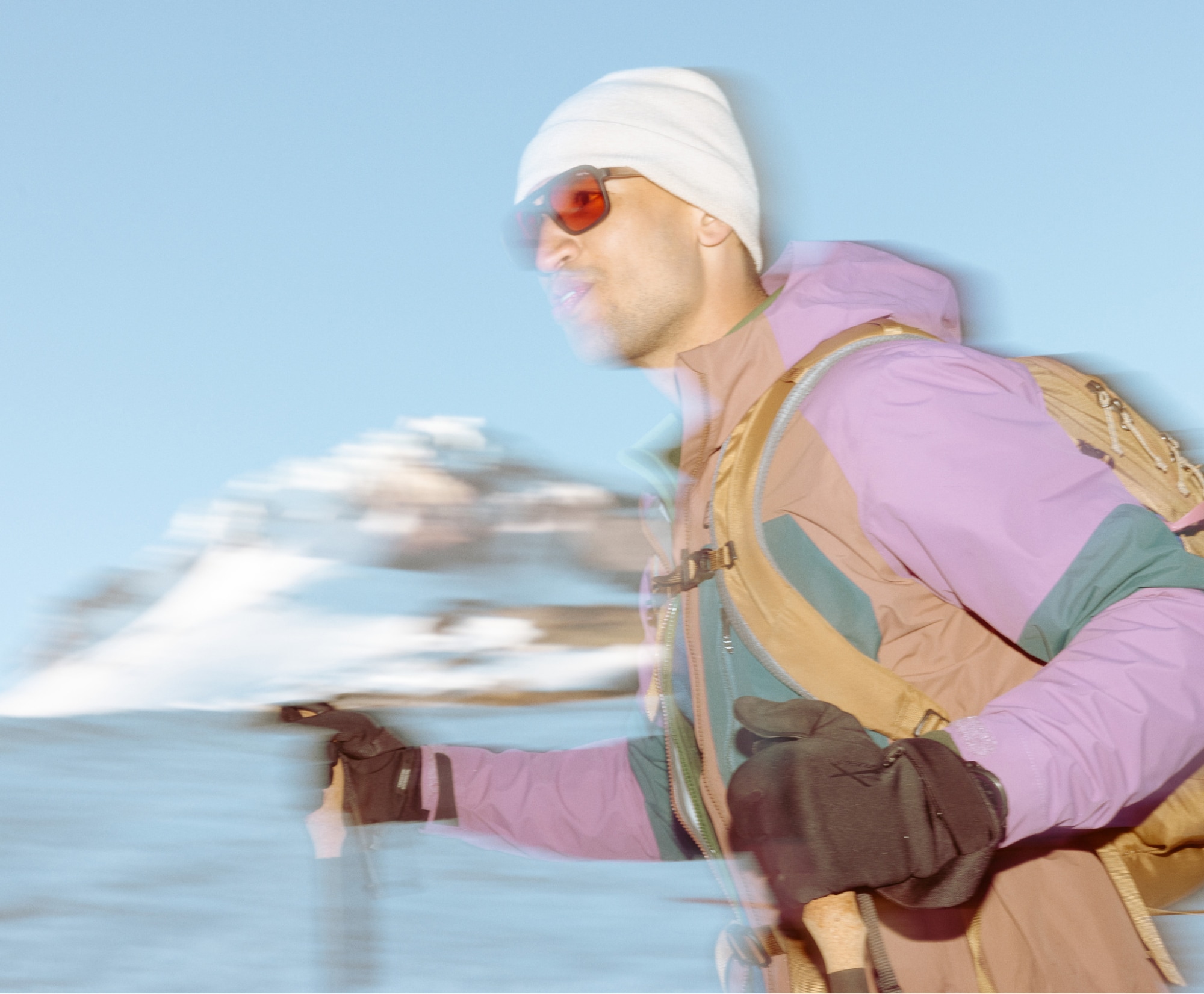 A hiker wearing winter gear while trekking through snow with trekking poles.