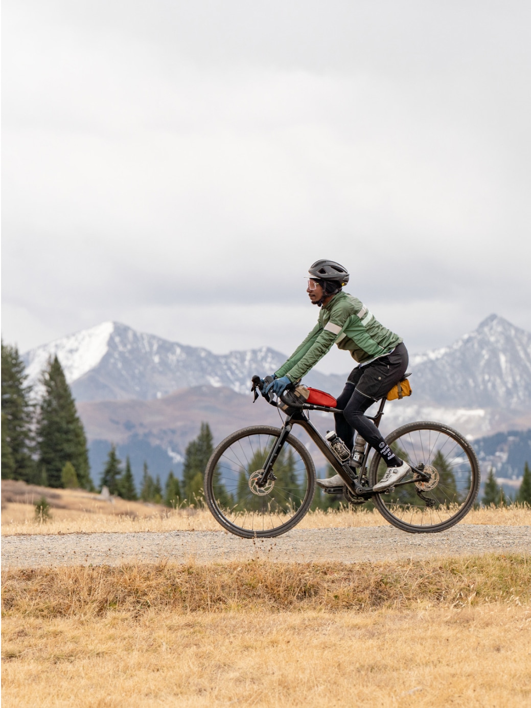 A mountain biker on a trail with snow-capped peaks in the background.