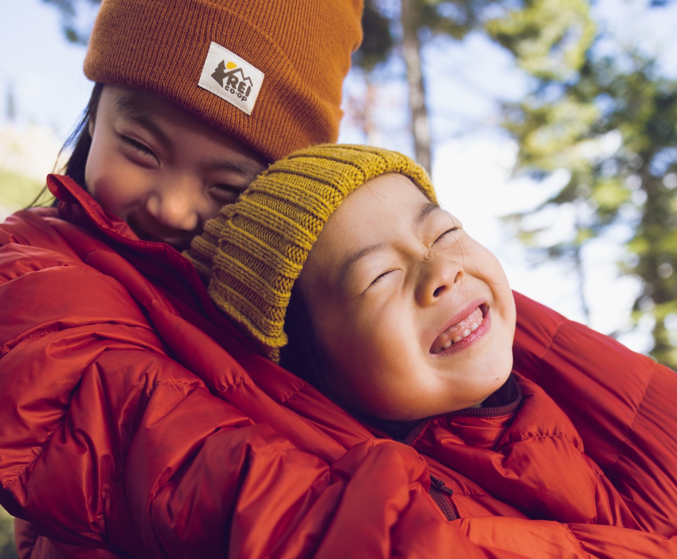 Two smiling kids wrapped up in a large coat.