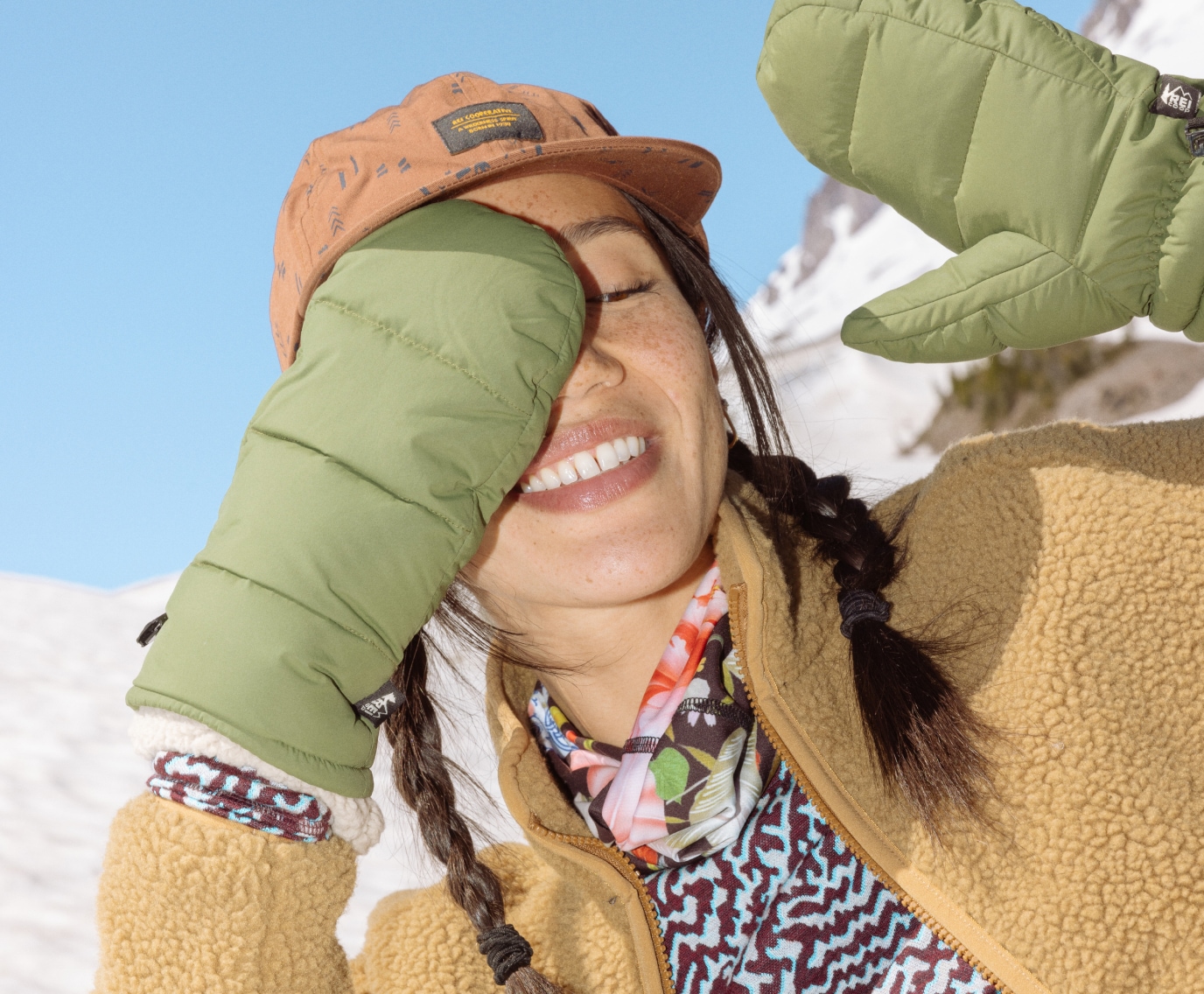 A person in winter gear playfully covers their eyes with mittens.