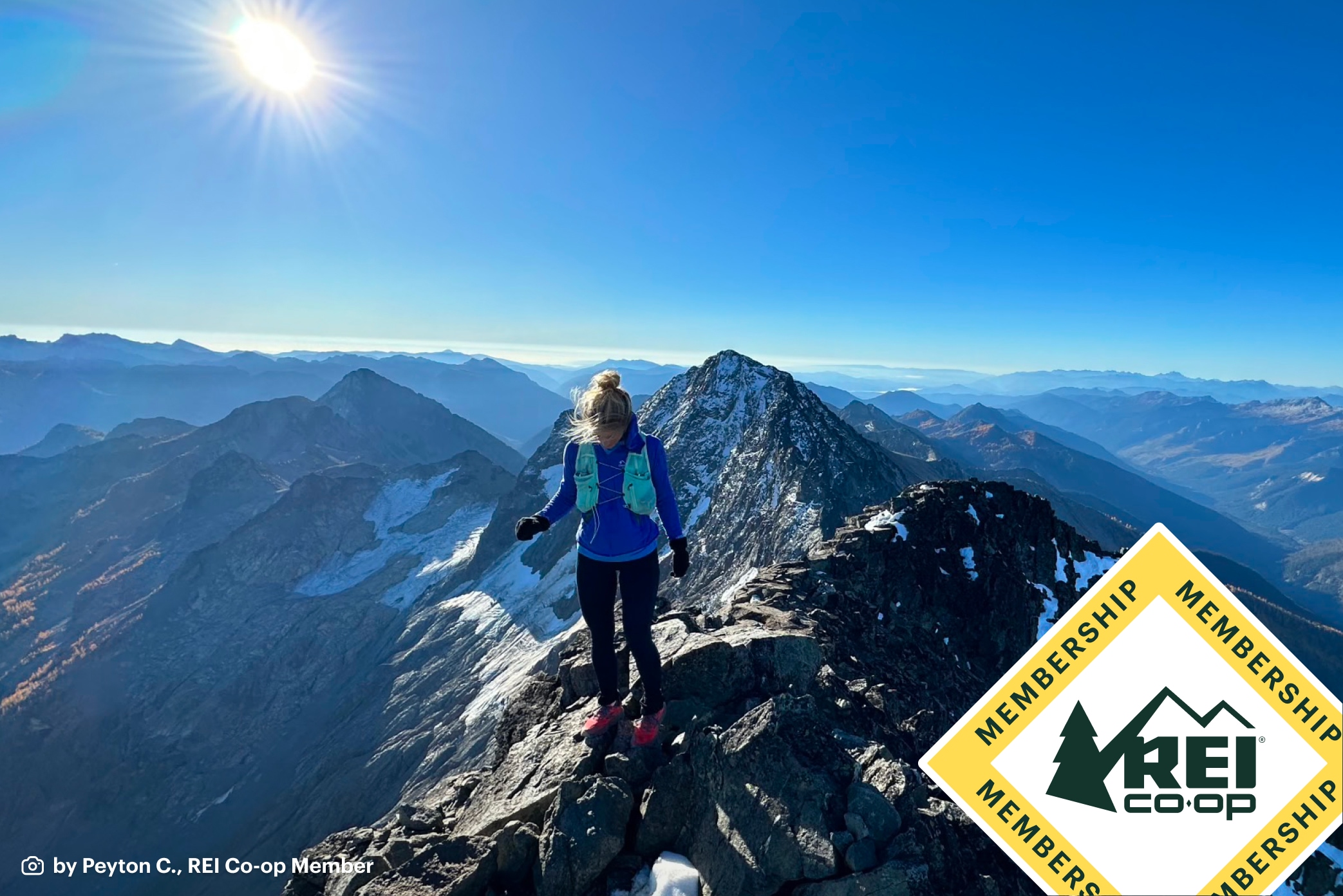 Triangular REI Co-op Member badge overlays a photo by REI Co-op Member Peyton C. of a hiker traversing an alpine ridge under a sunny bluebird sky.