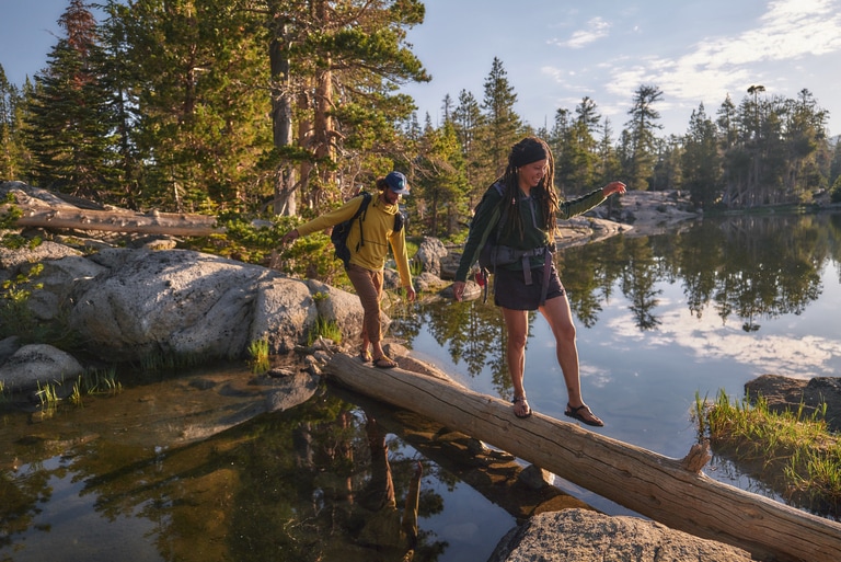 Two people walk across a body of water on an overturned log.