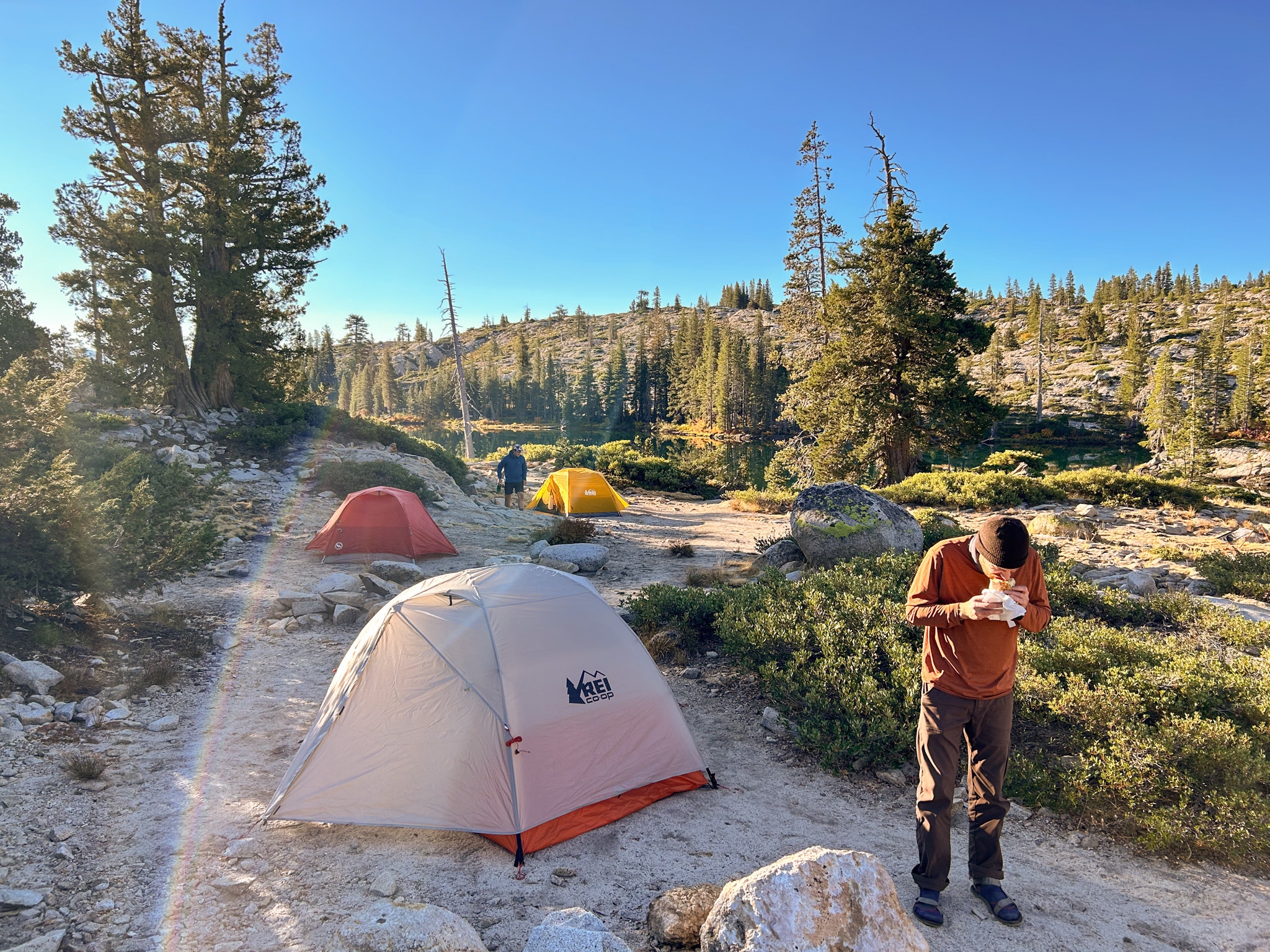 A person enjoys a burrito at a campsite with three tents in the background.