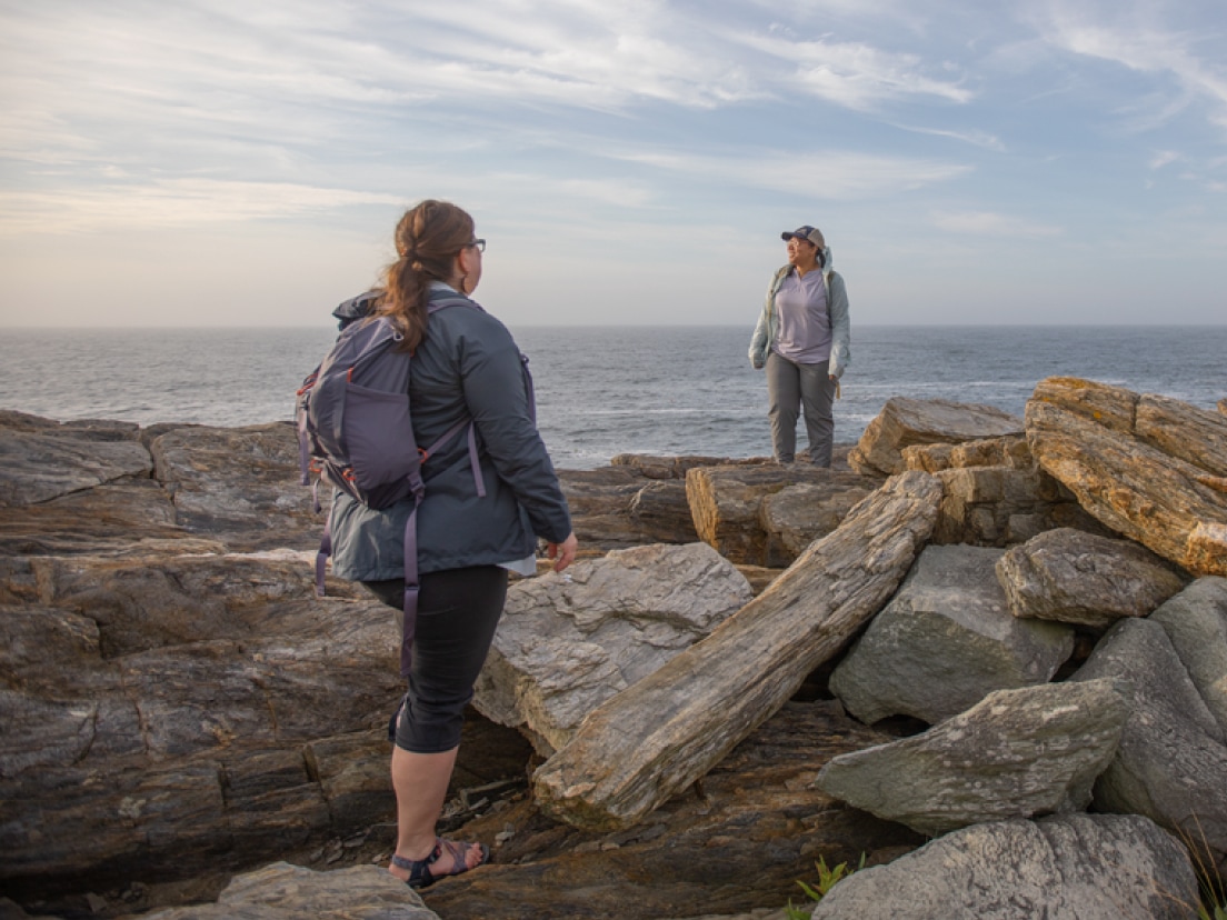 Two friends stand atop a pile of rocks while they take in the view.