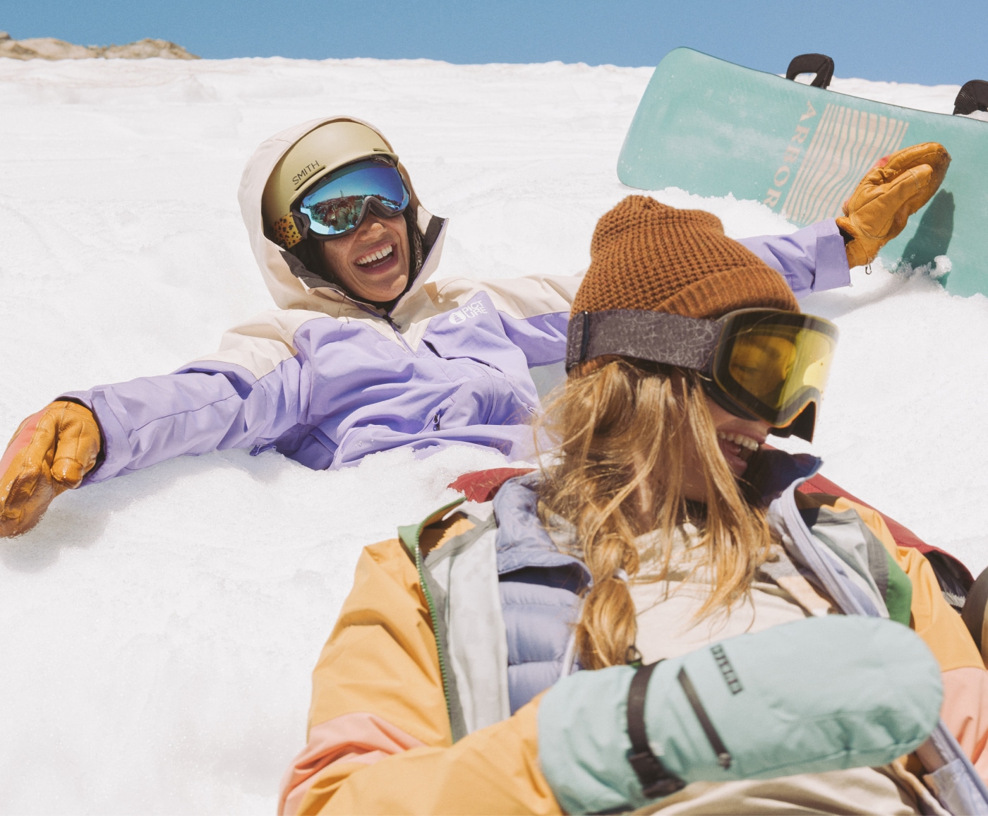 Two snowboarders playfully laugh in the snow.