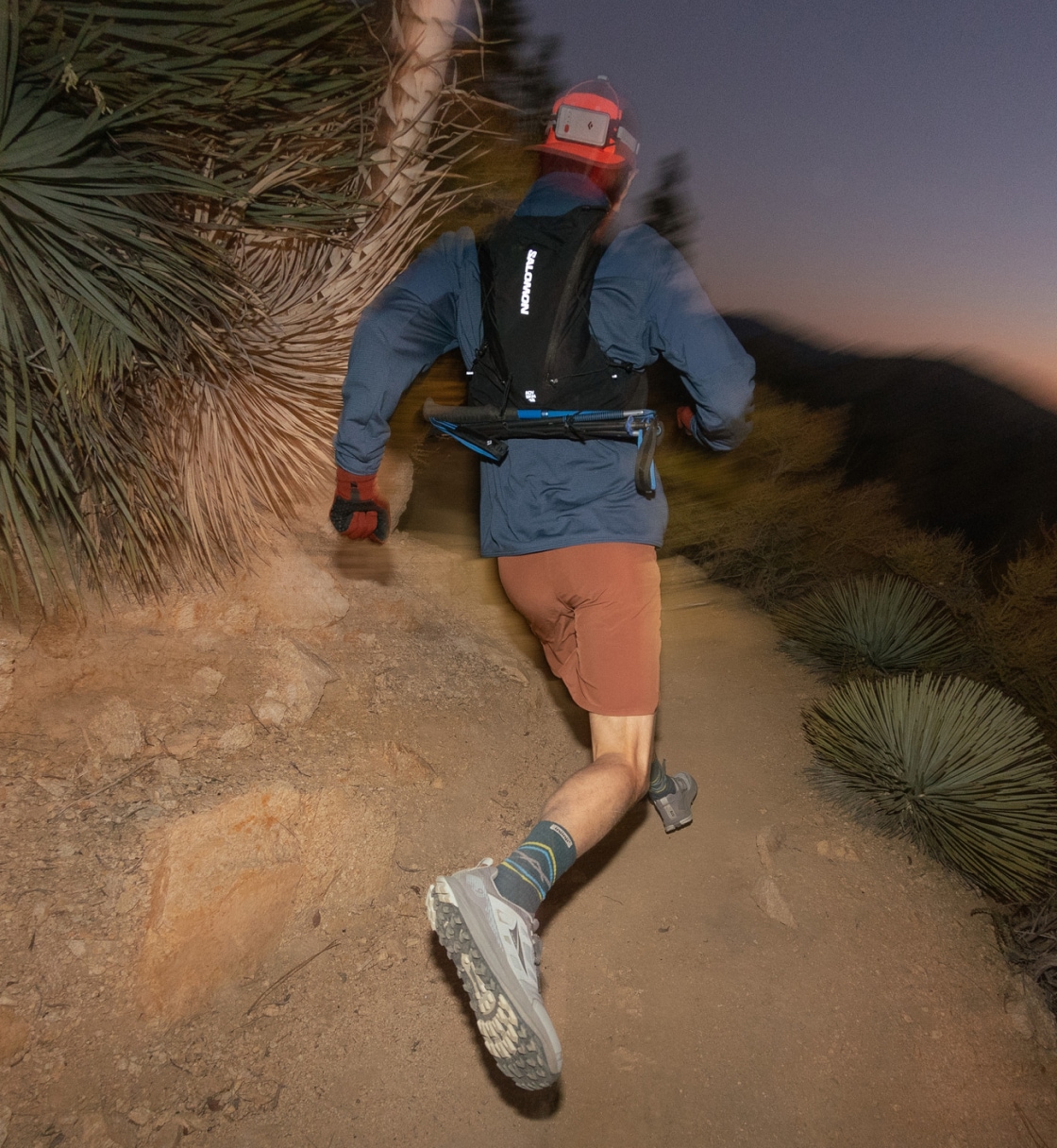 A trail runner zips up rocky terrain while the sun sets.