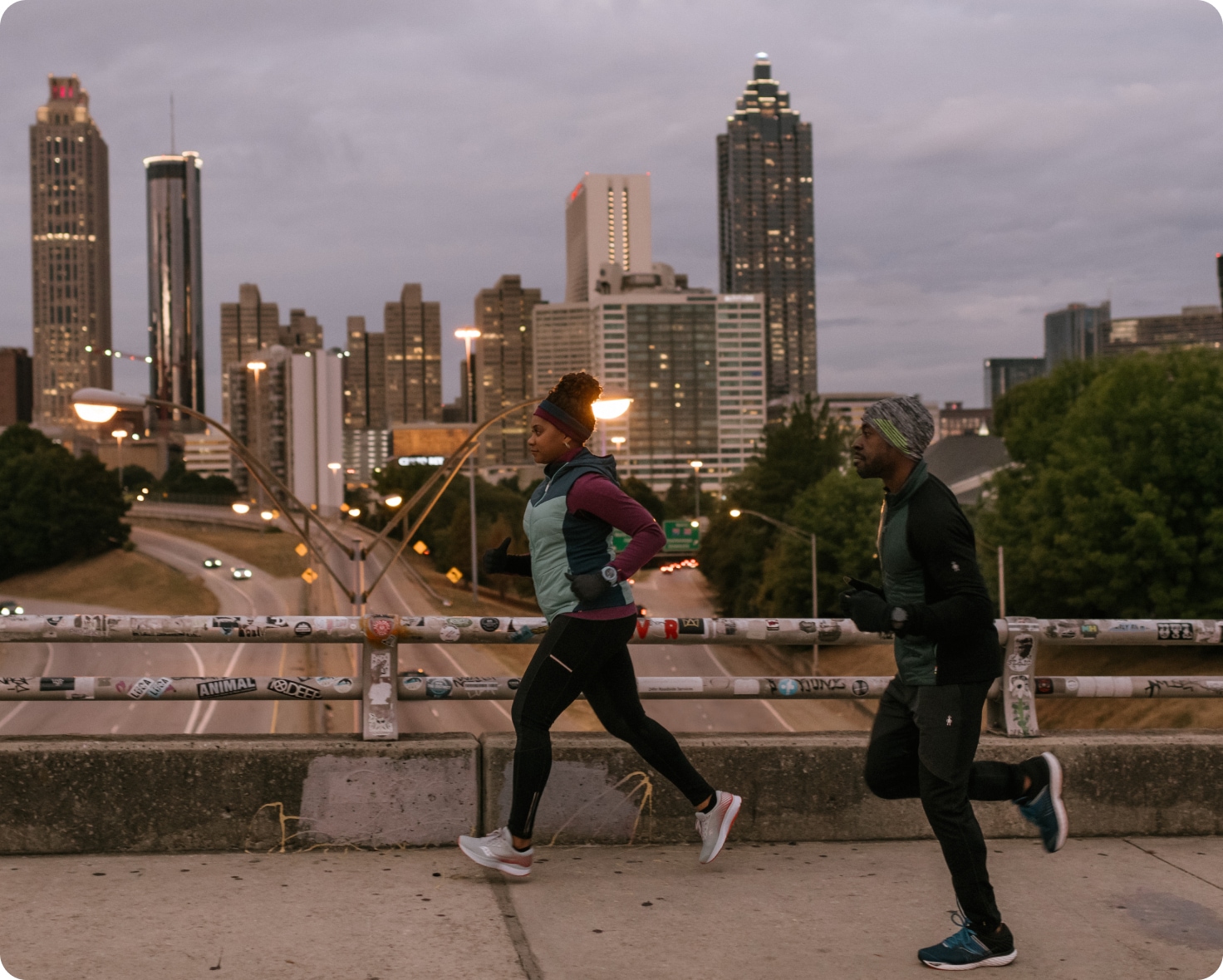 Two people run across a bridge in a city.