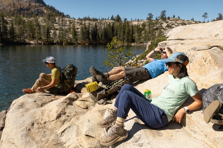 Three people lounge on rocks in the sun by a body of water.