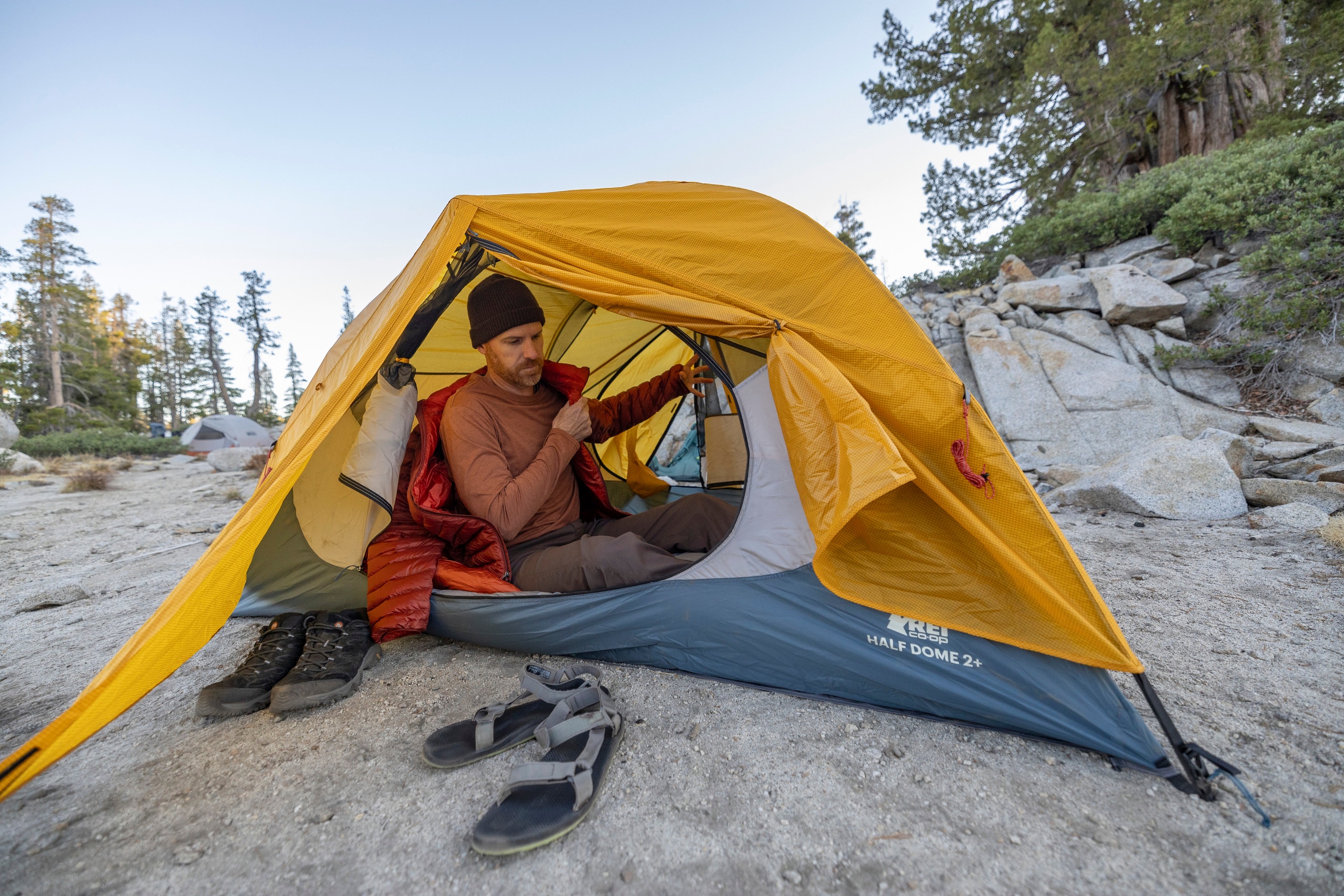 A person huddles inside an orange and blue backpacking tent.