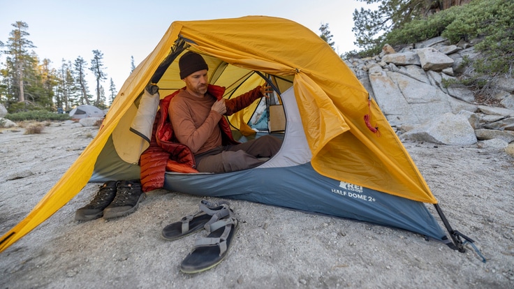 A person huddles inside an orange and blue backpacking tent.