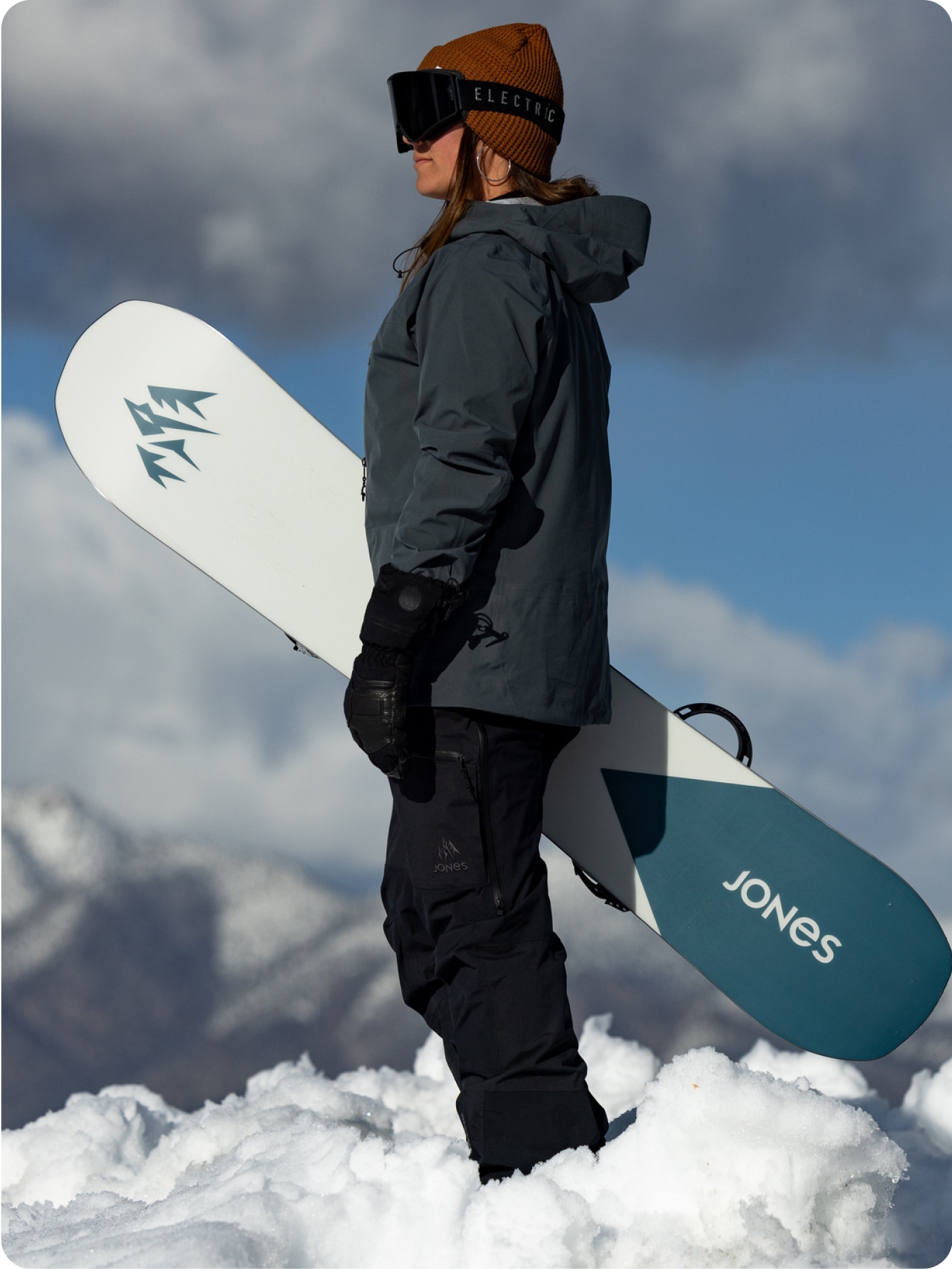 A person stands in the snow with their Jones snowboard.