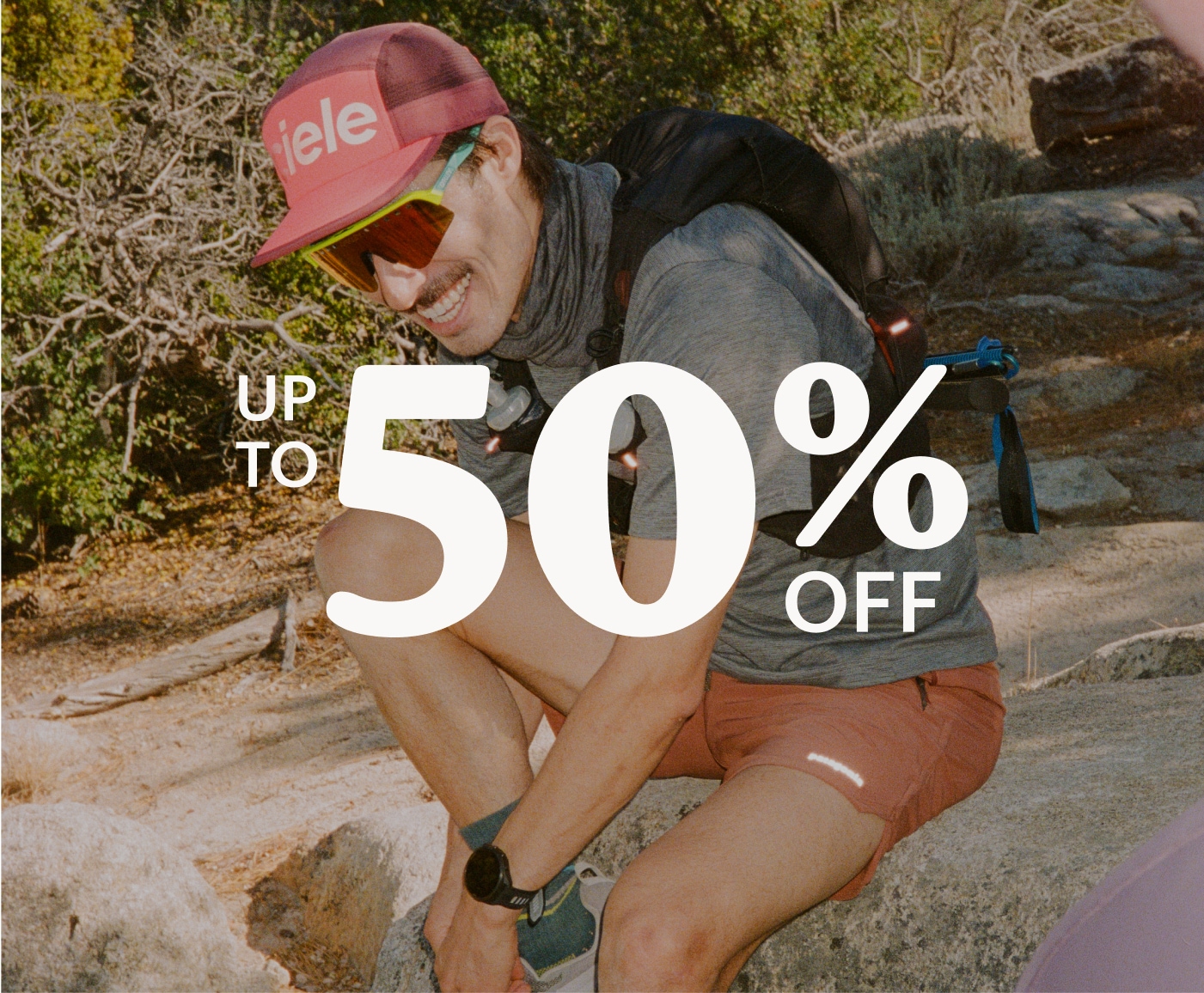 Up to 50% off. A runner happily ties their shoe while smiling for the camera.