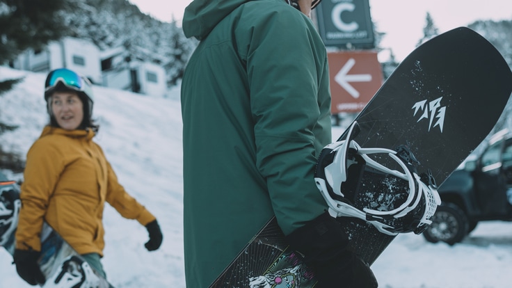 Two people carry their snowboards at a ski area