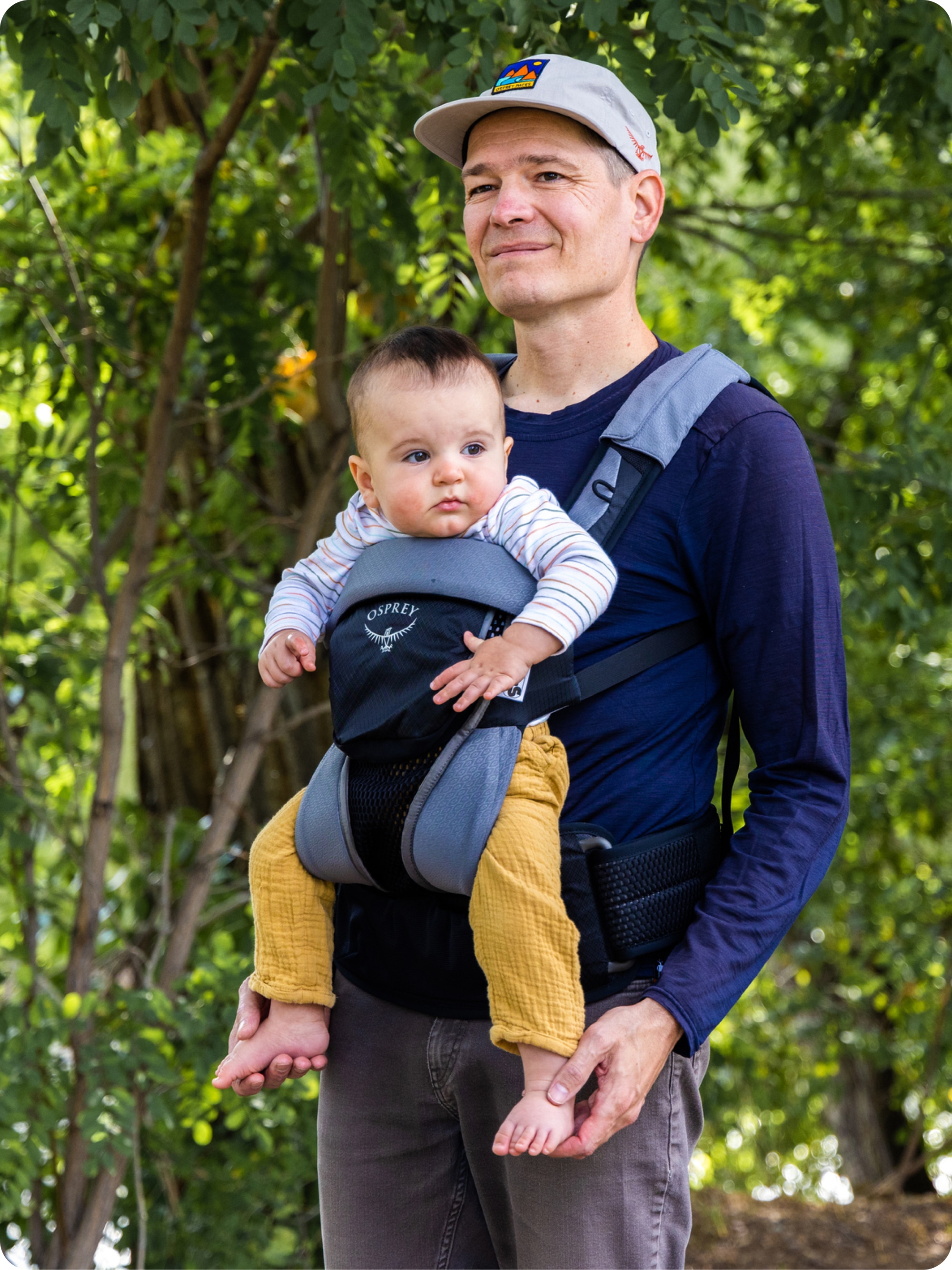 A person enjoys a forest walk with a baby in an Osprey carrier.