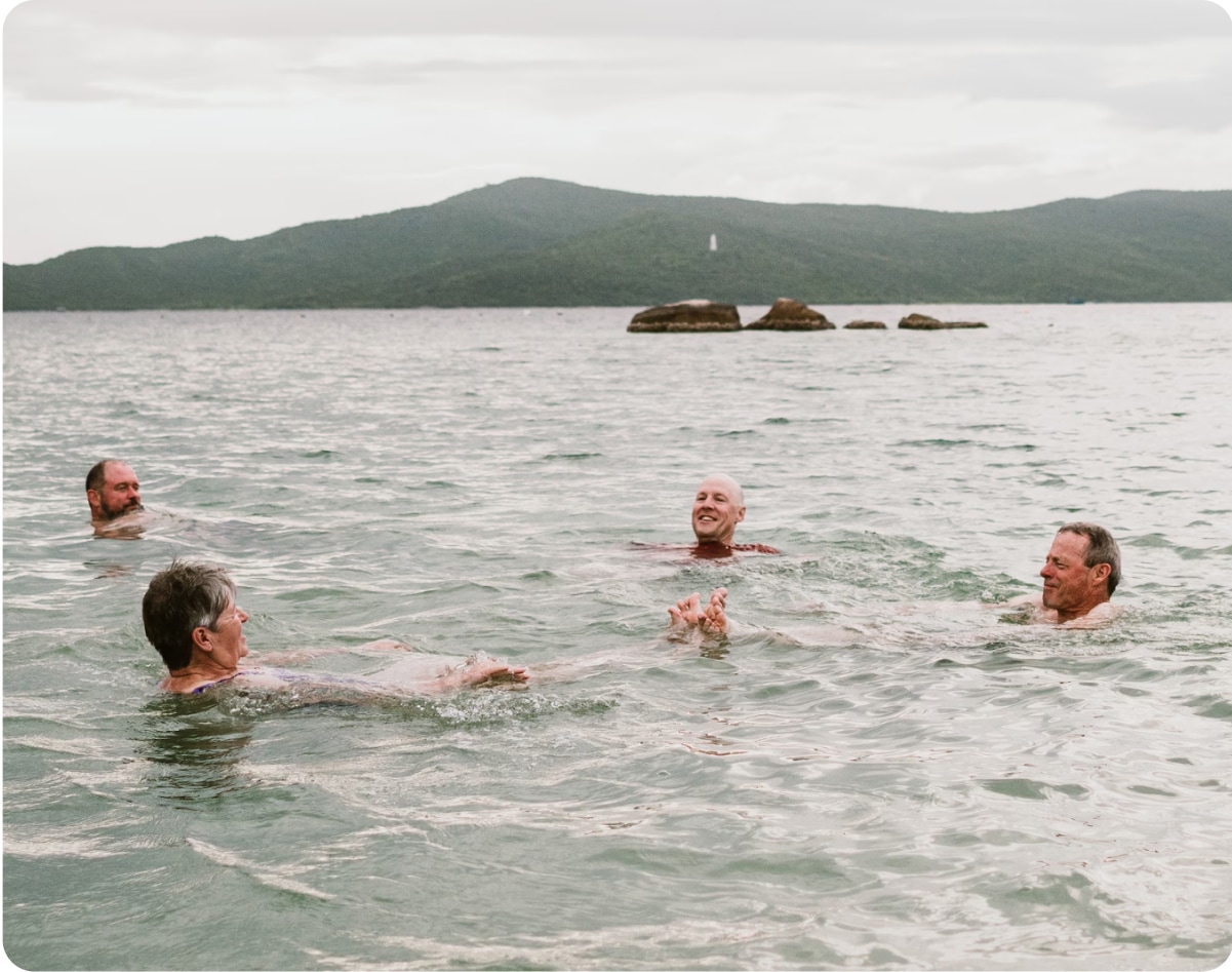 Four people relaxing in a body of water with mountains in the background.