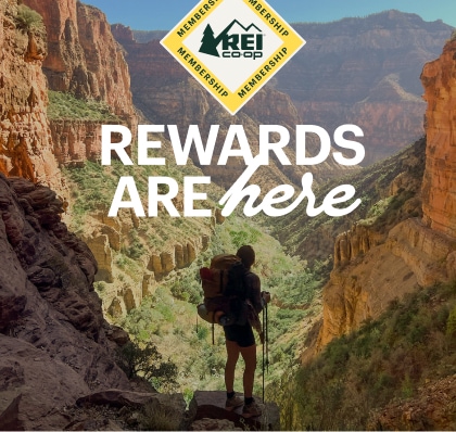 R E I Co-op membership. Rewards are here. A hiker stands on a rock and looks out over a canyon.