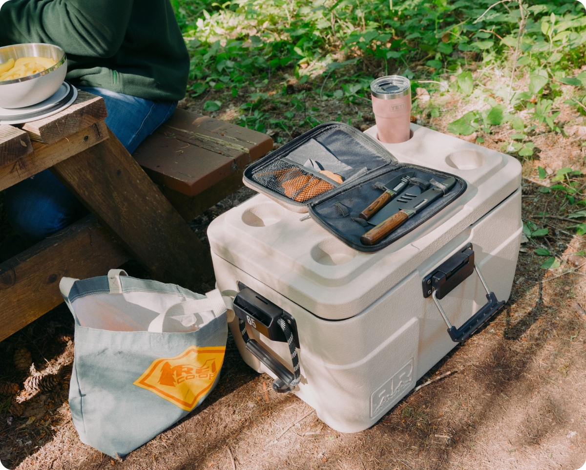 A set of camp dinnerware and a YETI tumbler sitting on top of a cooler.