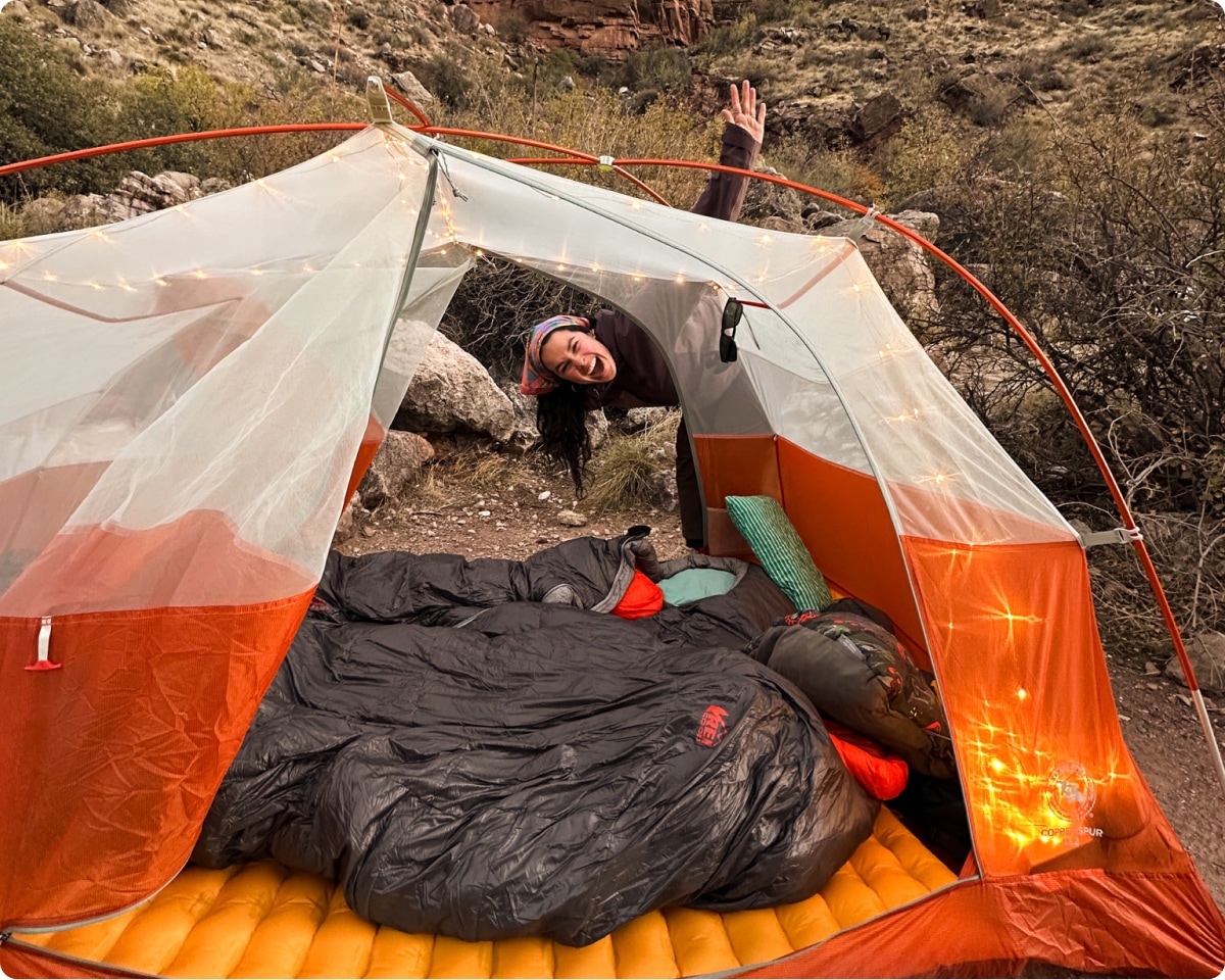 A camper smiles for the camera while posing with their tent.