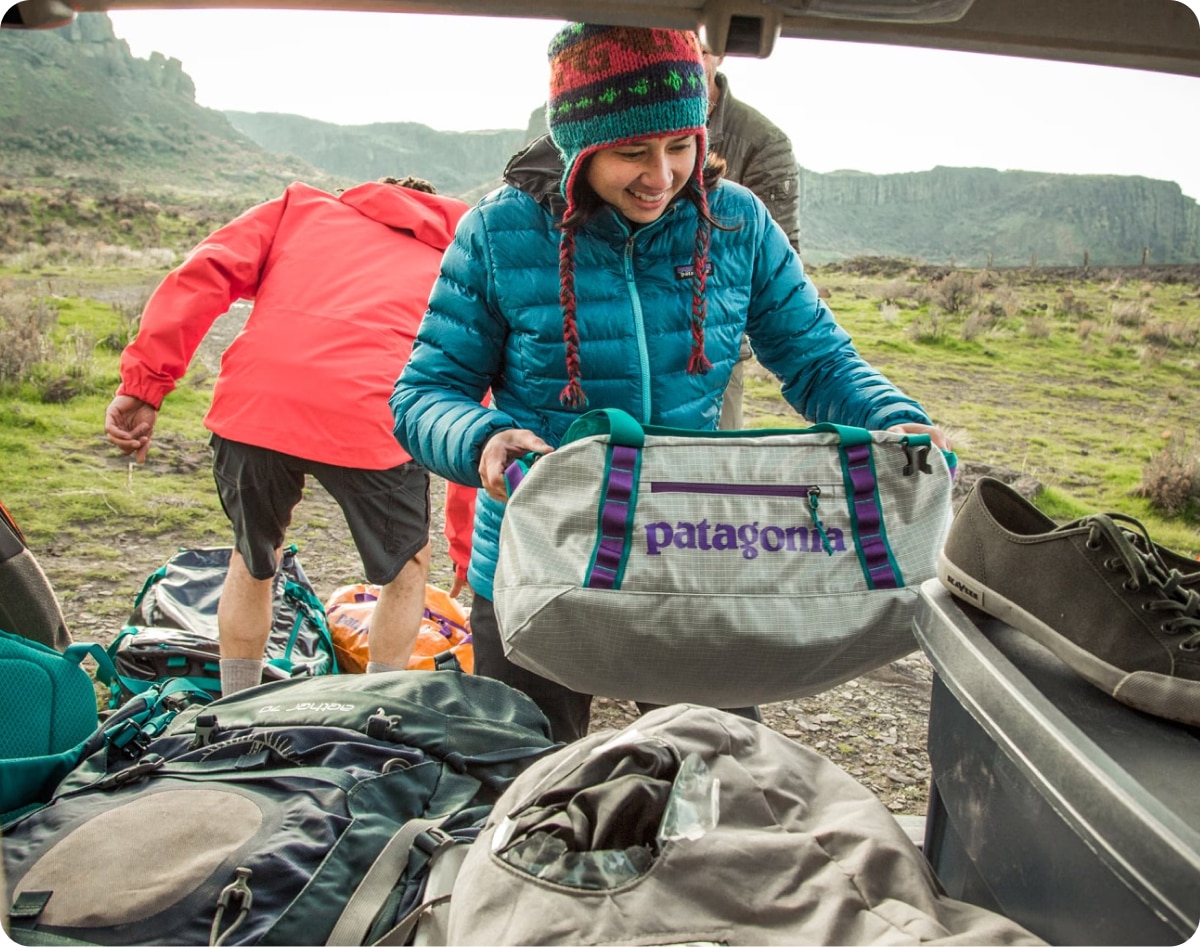 A person puts their Patagonia duffel bag into their trunk after a camping trip.