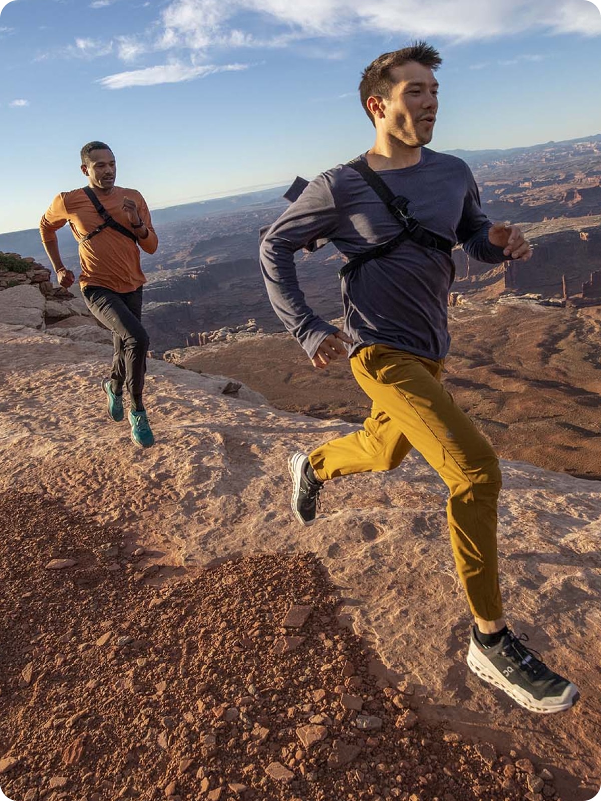 Two people running across a rocky trail together.