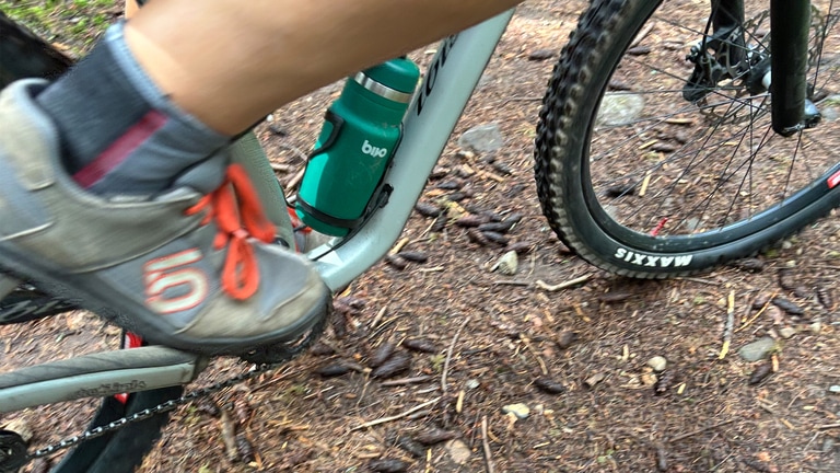 A close up photo of a person wearing grey mountain bike shoes on a dirt trail