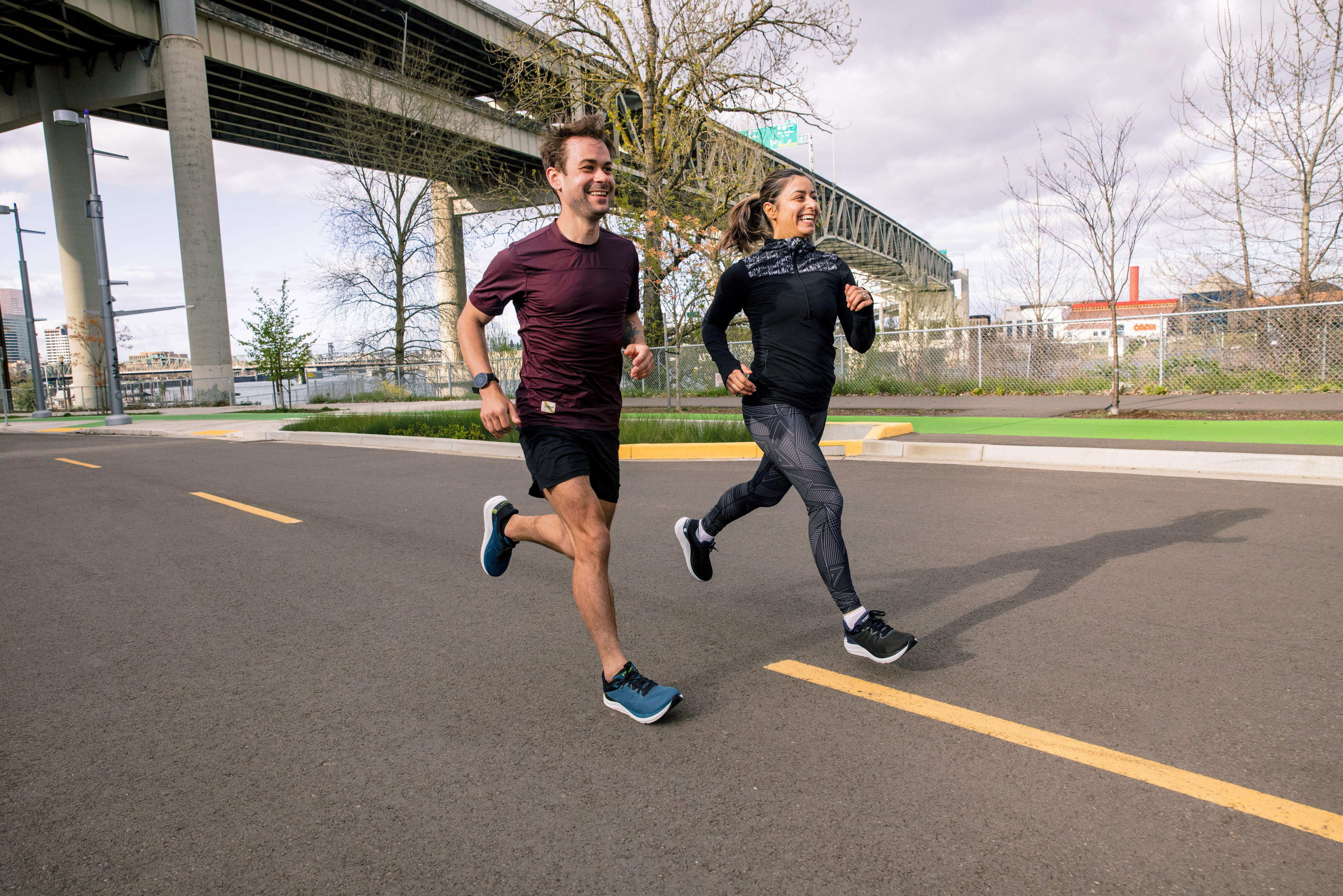 A man and a woman run on the road near a bridge.