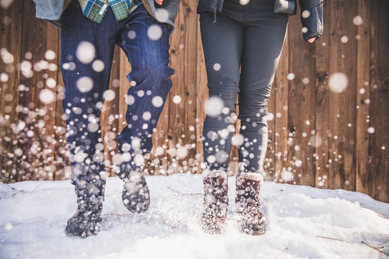 Two people jumping in the snow, kicking snow toward the camera