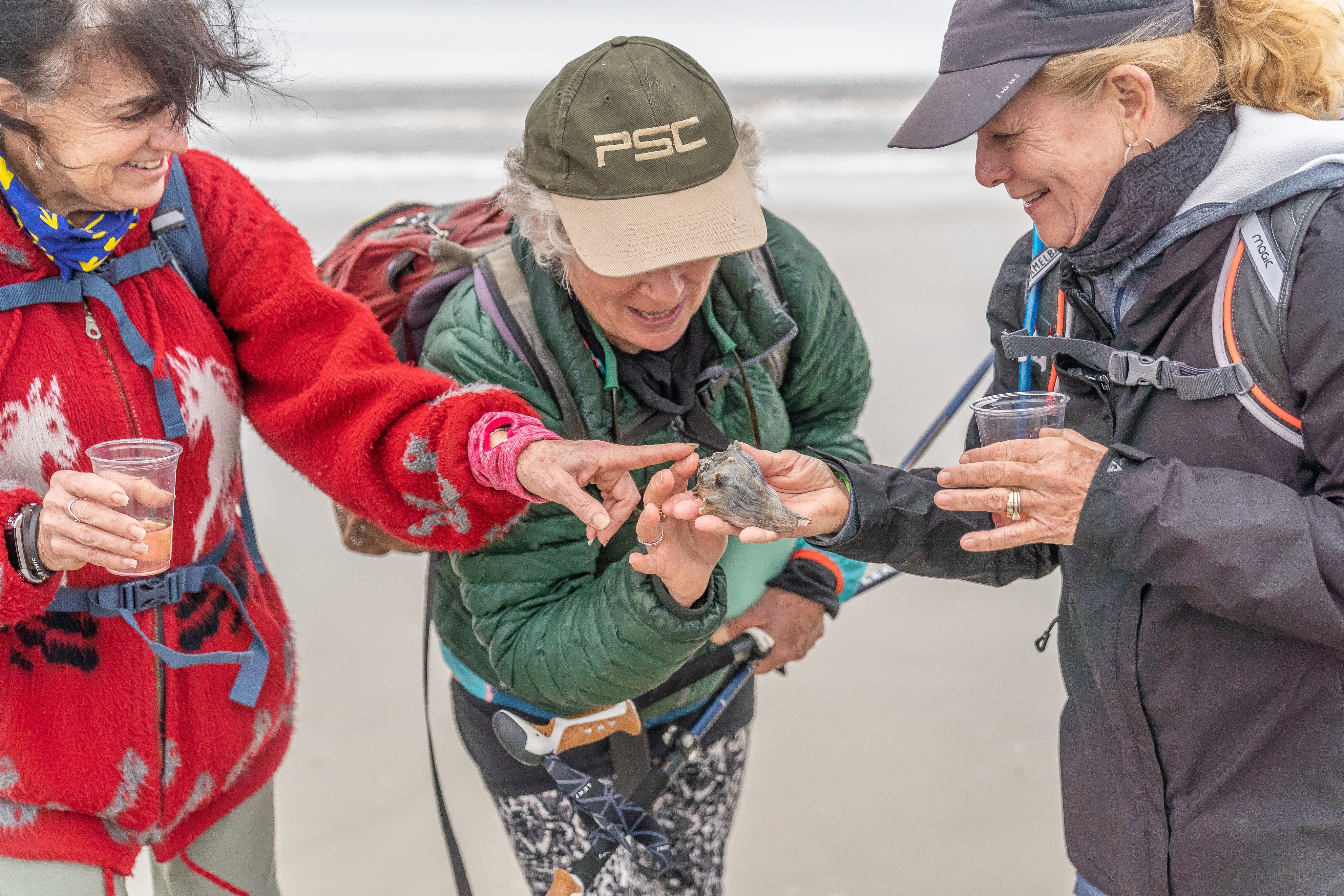 Three people stop their walk to look at a shell they found along the beach.