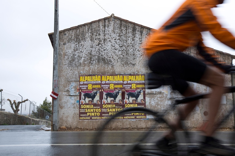 person biking on a wet road past a building