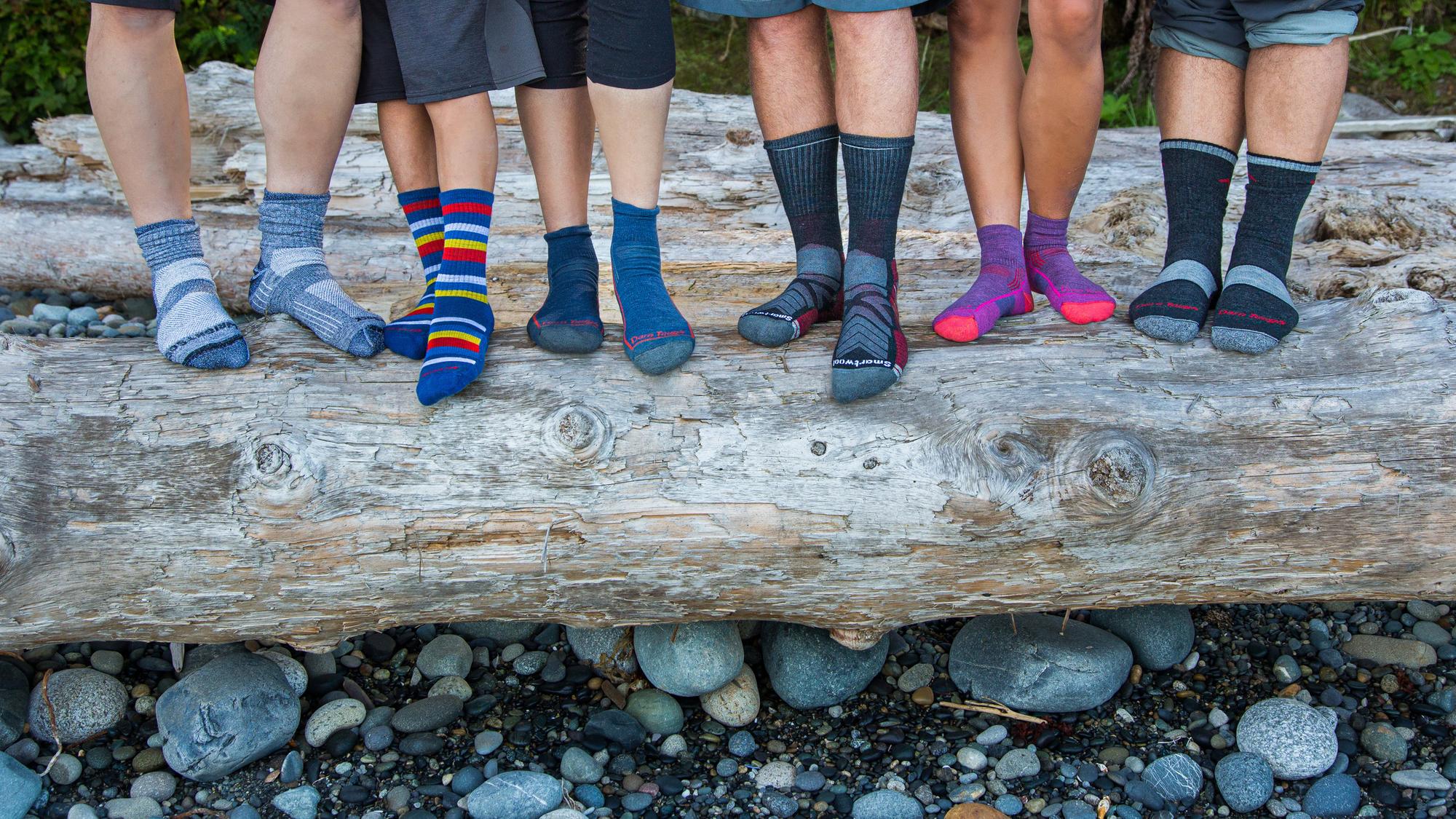 Six hikers stand on a beach log displaying their socks