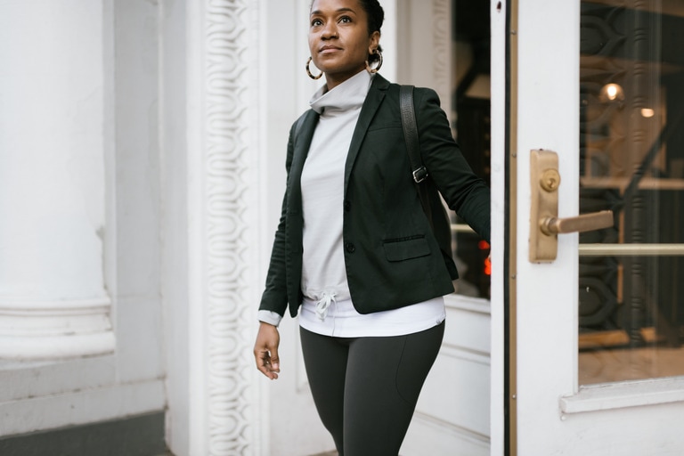 A woman wearing a blazer jacket over a stylish athleisure sweatshirt and yoga pants.