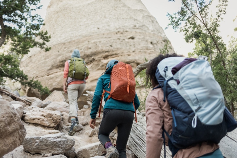 Three people hike up a craggy rock face, away from the camera.