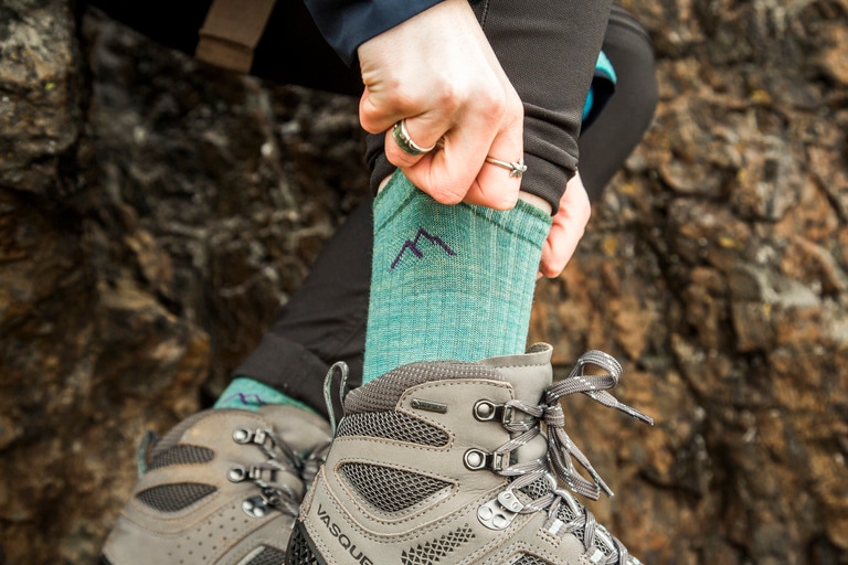 A person wearing hiking boots pulls up their Darn Tough socks.