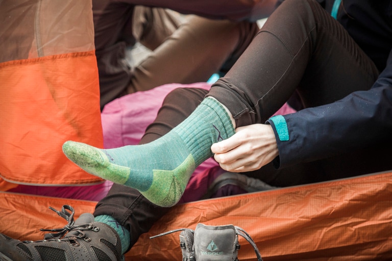 A person sitting in a tent pulls on a pair of green socks with light-green heal and toe segments.