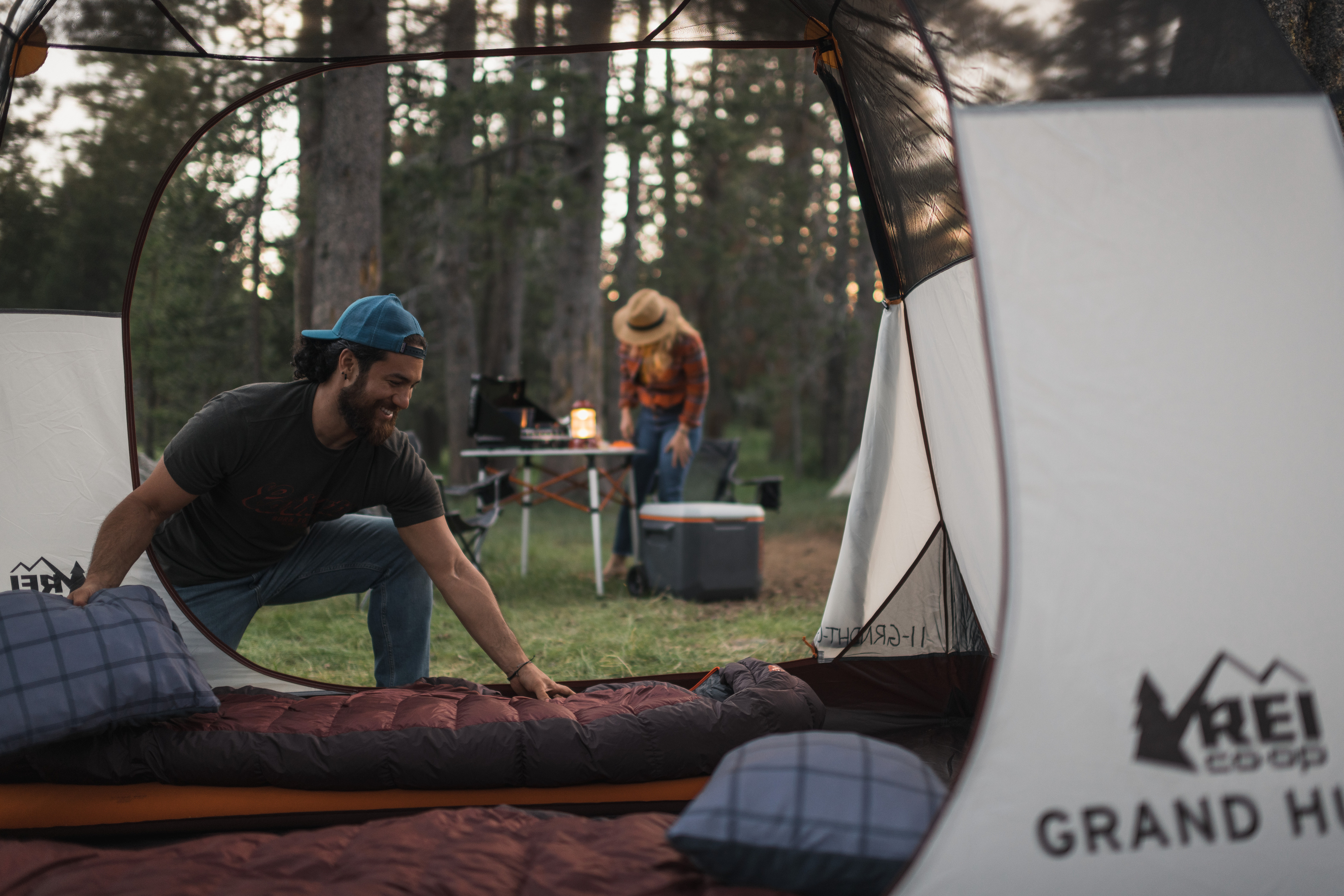 A person spreads out a sleeping bag inside a tent at a camping site