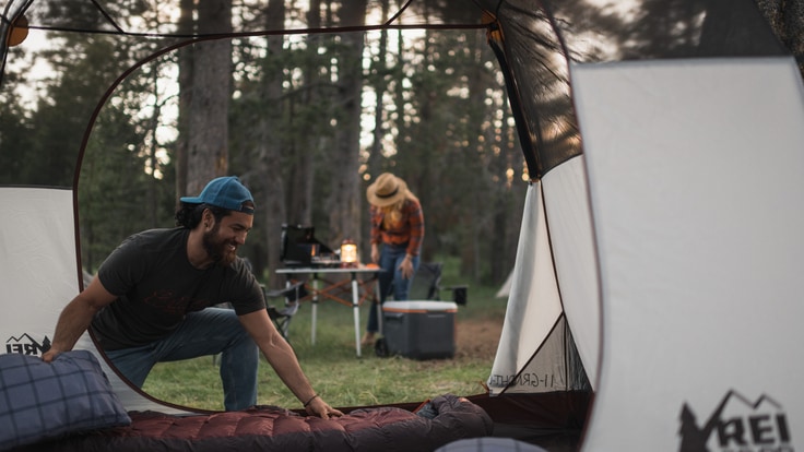 A person spreads out a sleeping bag inside a tent at a camping site