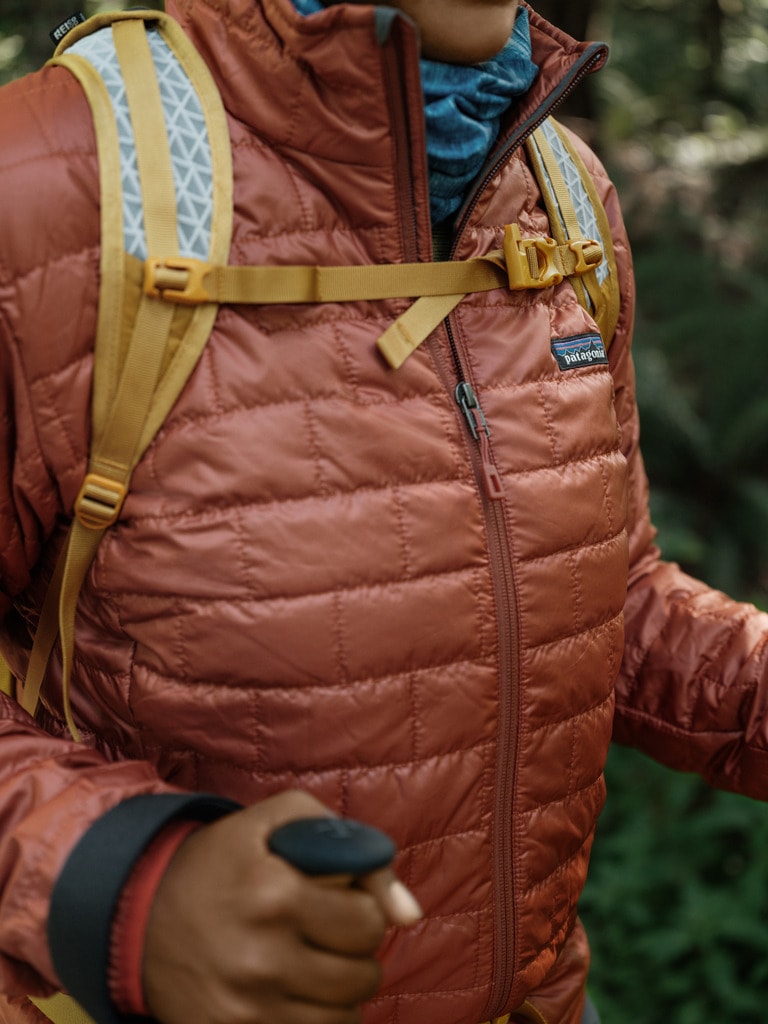 A close up of a hiker wearing a puffy coat and holding hiking poles.